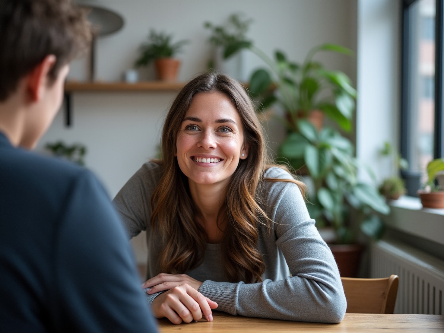 Vrouw aan een houten eettafel in gesprek, met een rustige uitdrukking, in een licht Nederlands interieur