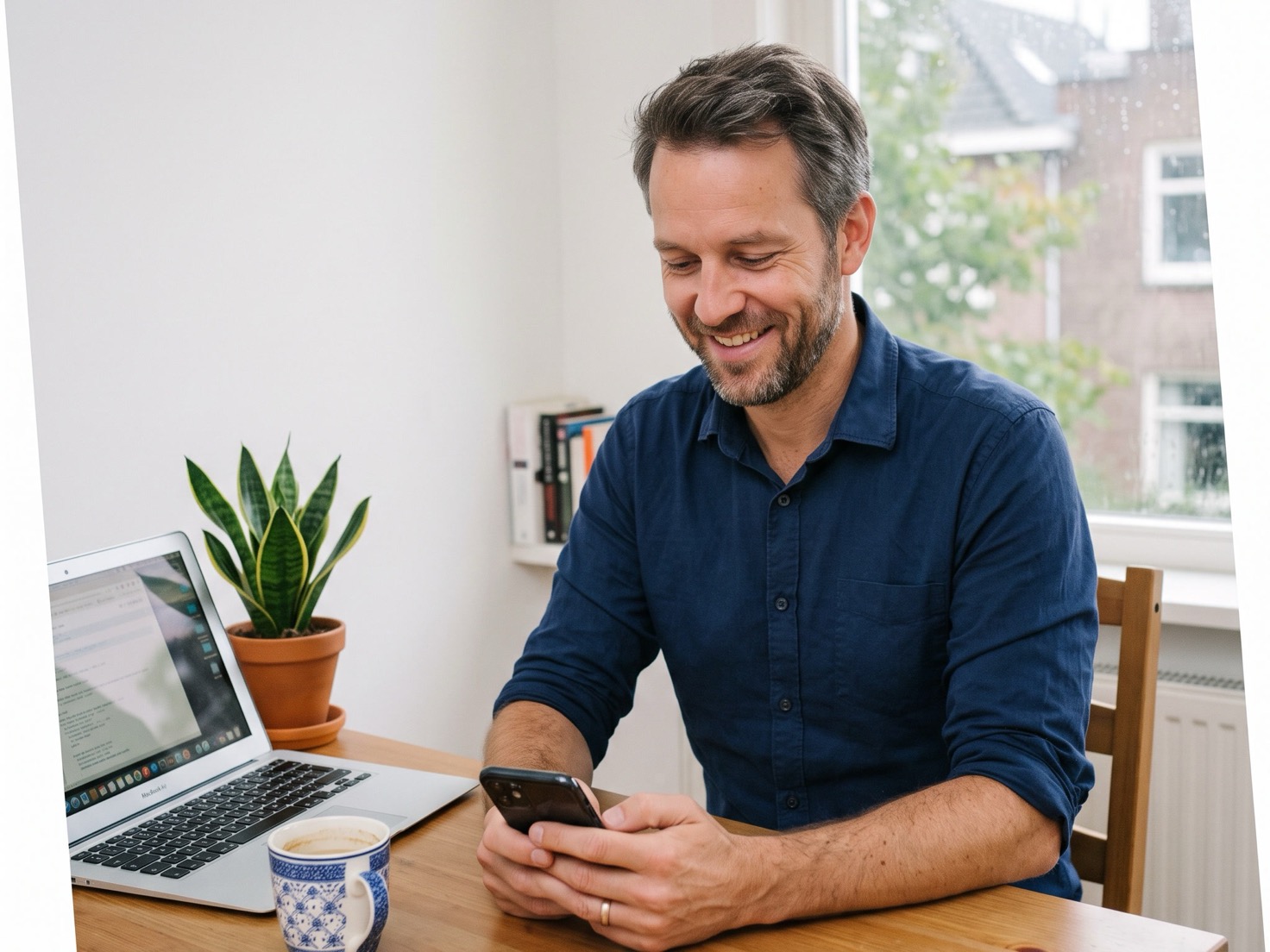 Solo-ondernemer bekijkt zijn telefoon aan een opgeruimde werktafel met open laptop