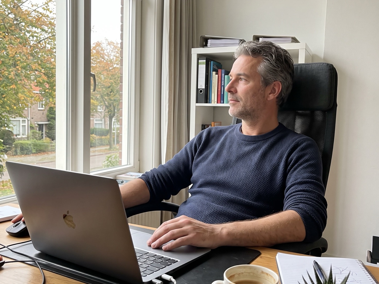 Man kijkt rustig weg van zijn laptop in zijn thuiswerkplek