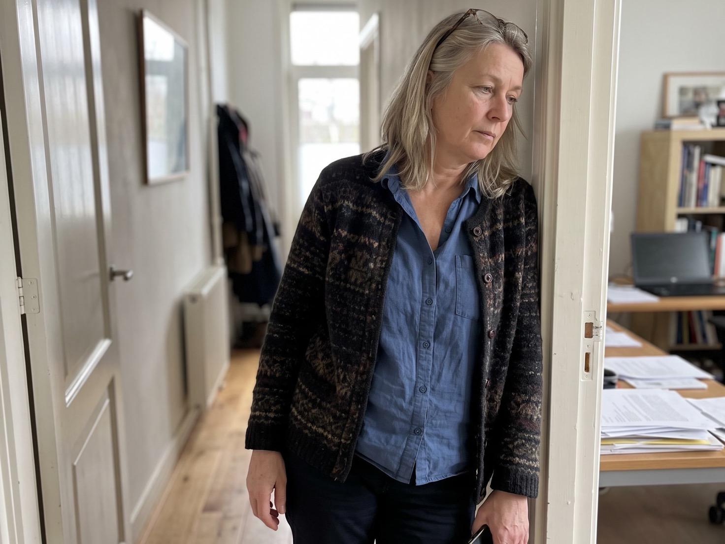 Vrouwelijke adviseur leunt in de deuropening van haar werkkamer met haar telefoon in de hand