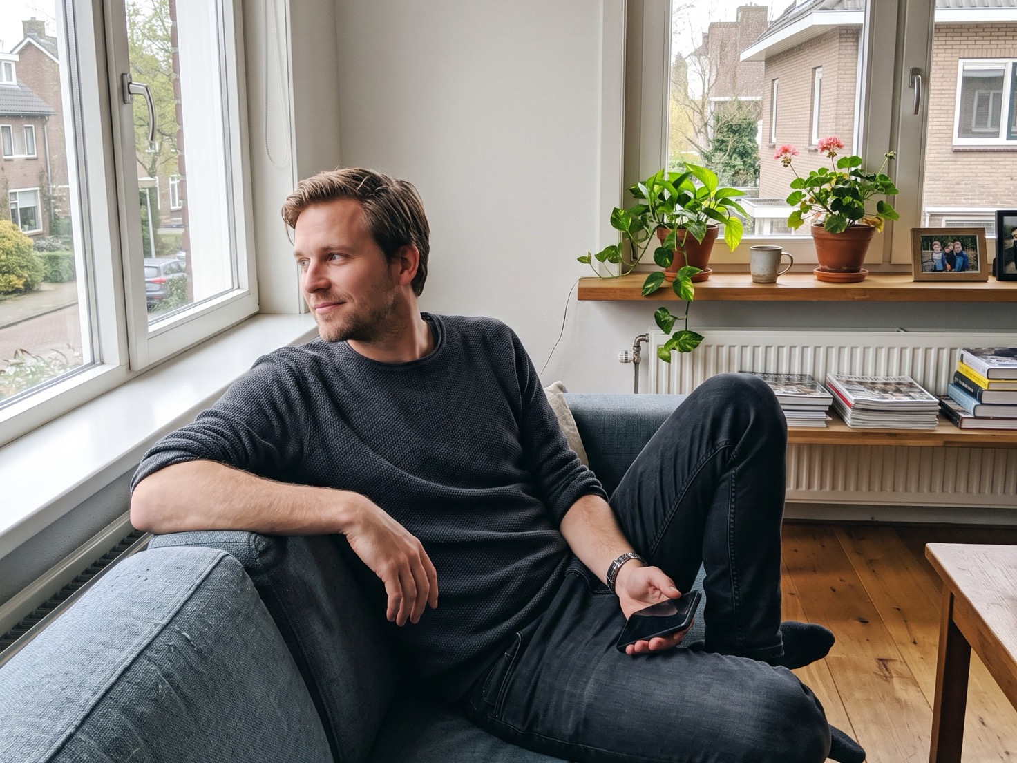 Solo-ondernemer ontspannen op de bank in de woonkamer, telefoon losjes in de hand, net een tevreden berichtje van een klant gelezen.