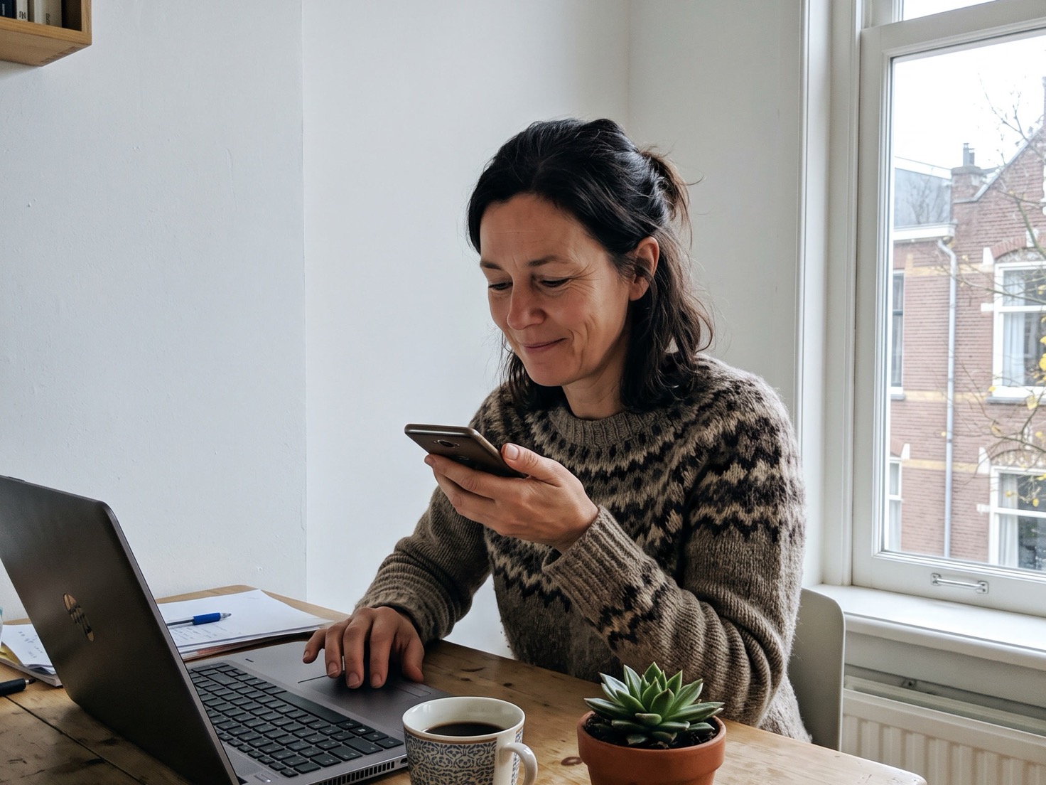 Vrouw luistert op haar telefoon terug naar een audiobericht aan haar werktafel