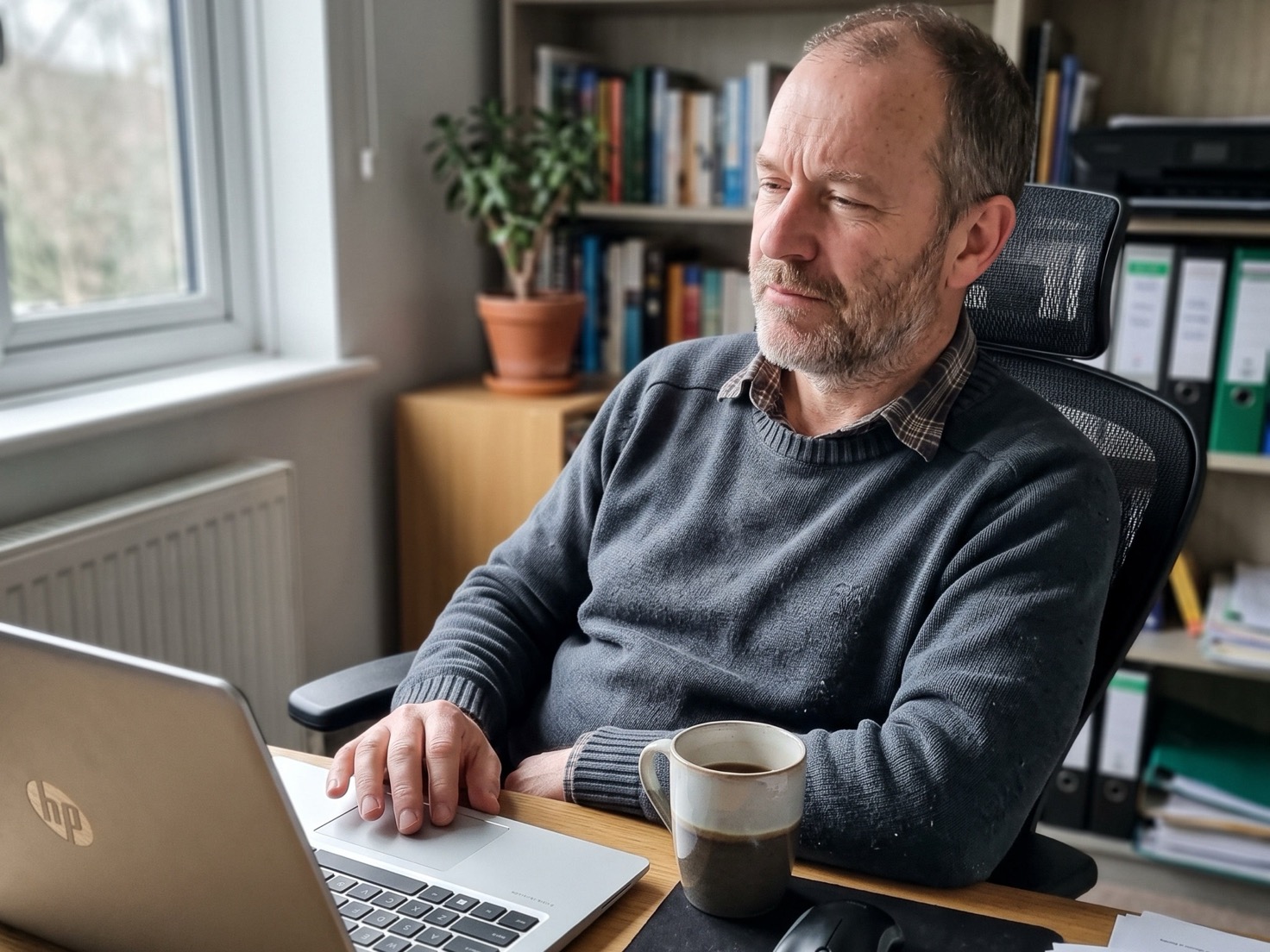 Ondernemer leunt achterover achter zijn laptop thuis en denkt na over zijn tekst