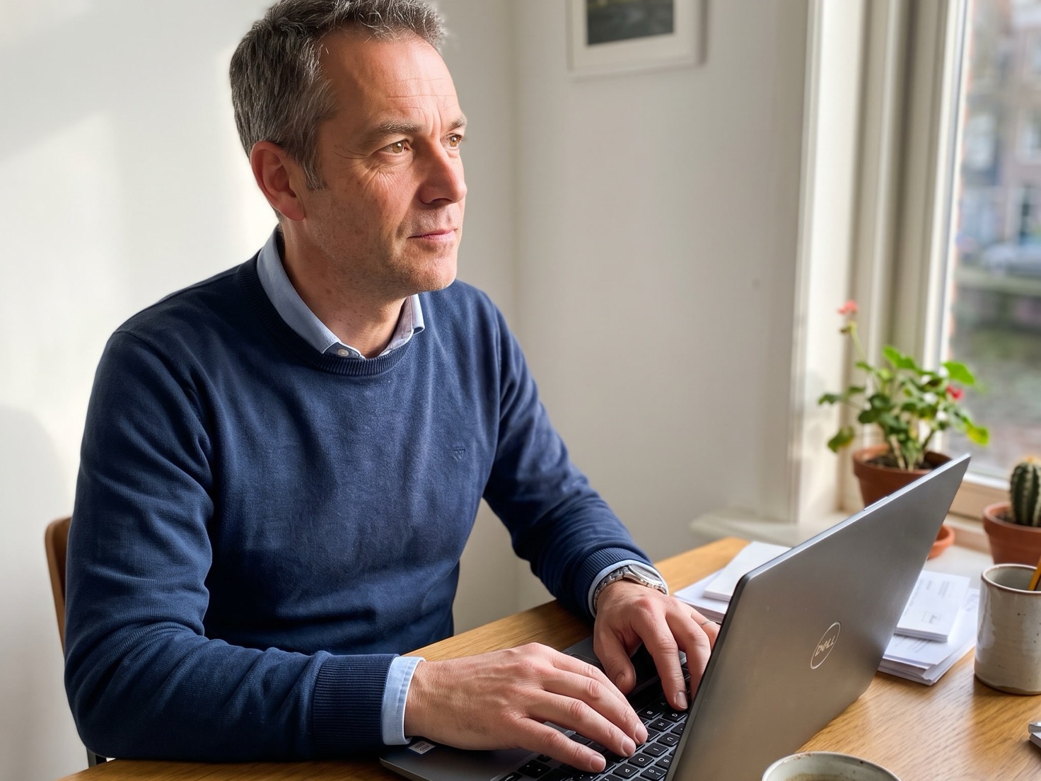 Solo-ondernemer werkt geconcentreerd achter een laptop aan zijn bureau bij het raam