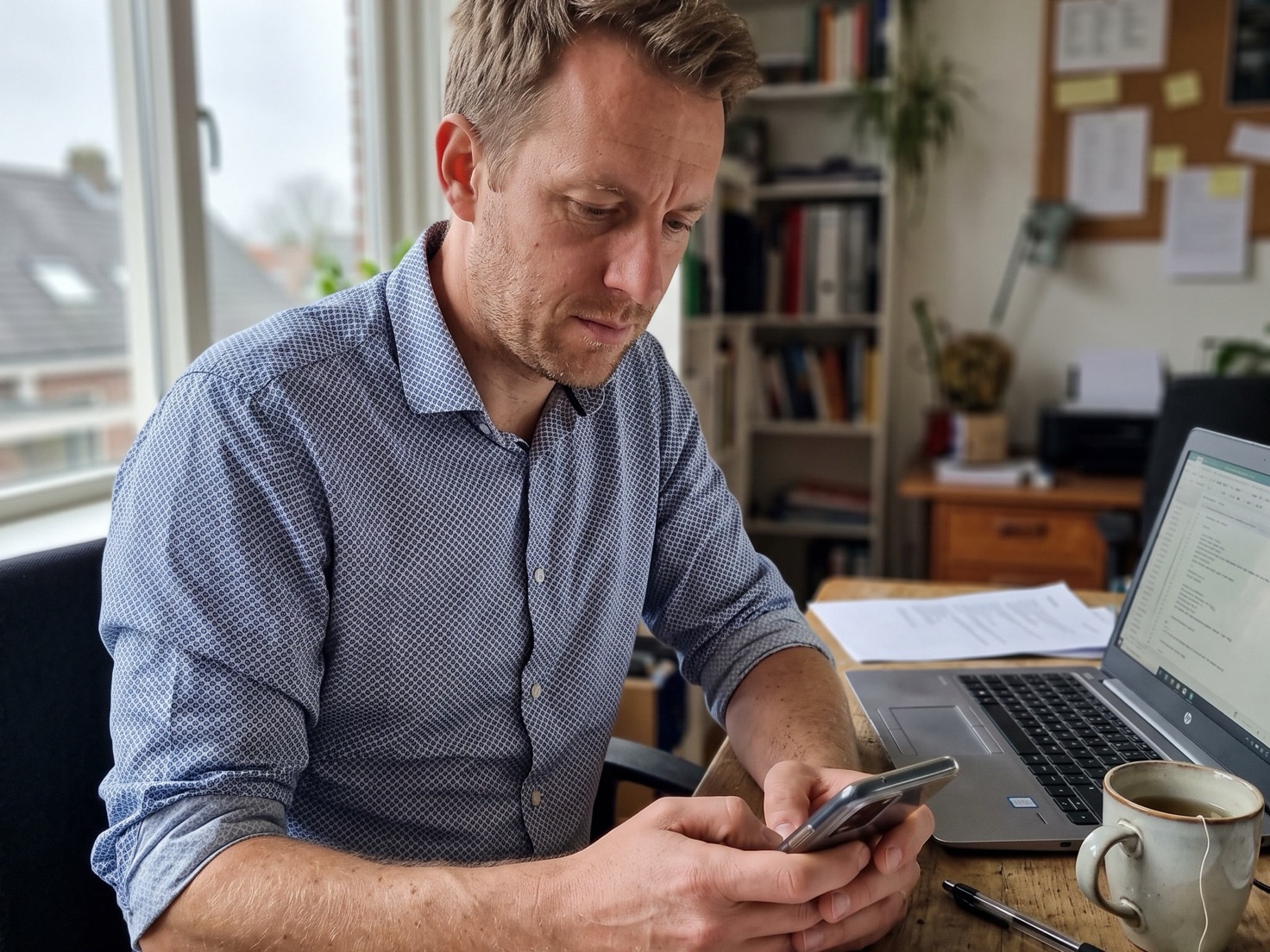 Ondernemer bekijkt aan zijn bureau zijn telefoon naast een open laptop