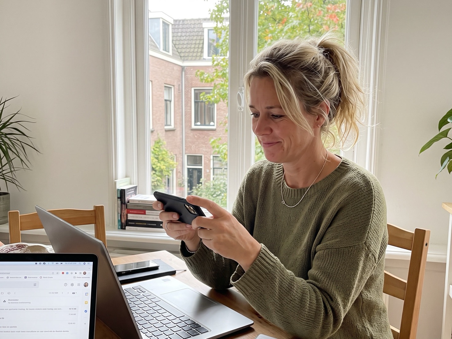 Vrouw leest een review op haar telefoon aan haar werktafel, laptop ernaast